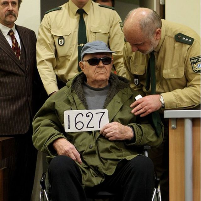 John Demjanjuk (centro) sostiene el número 1627, durante las etapas finales de su juicio en Mucnich, Alemania, 22 de febrero de 2011.